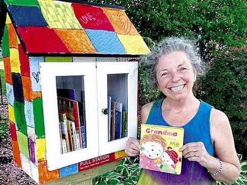 Jan stands next to a colorfully painted PULL station filled with books. She is smiling and holding up a picture book.